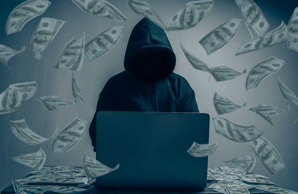 Hacker mit Laptop und Geldscheinen als Symbol für Cyberkriminalität